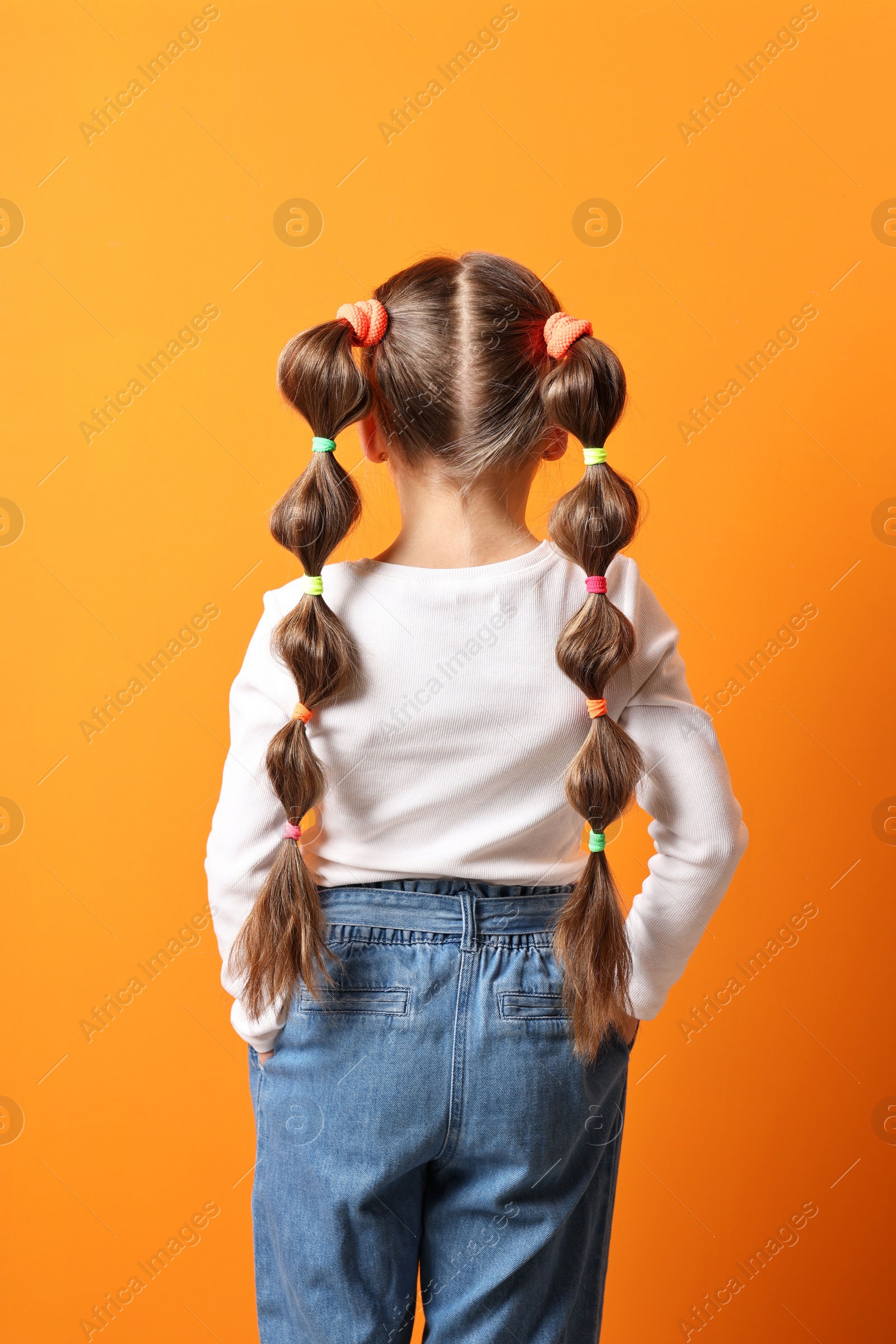 Photo of Little girl with beautiful hairstyle on orange background, back view