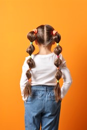 Photo of Little girl with beautiful hairstyle on orange background, back view