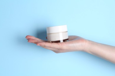 Woman holding jar of cream on light blue background, closeup