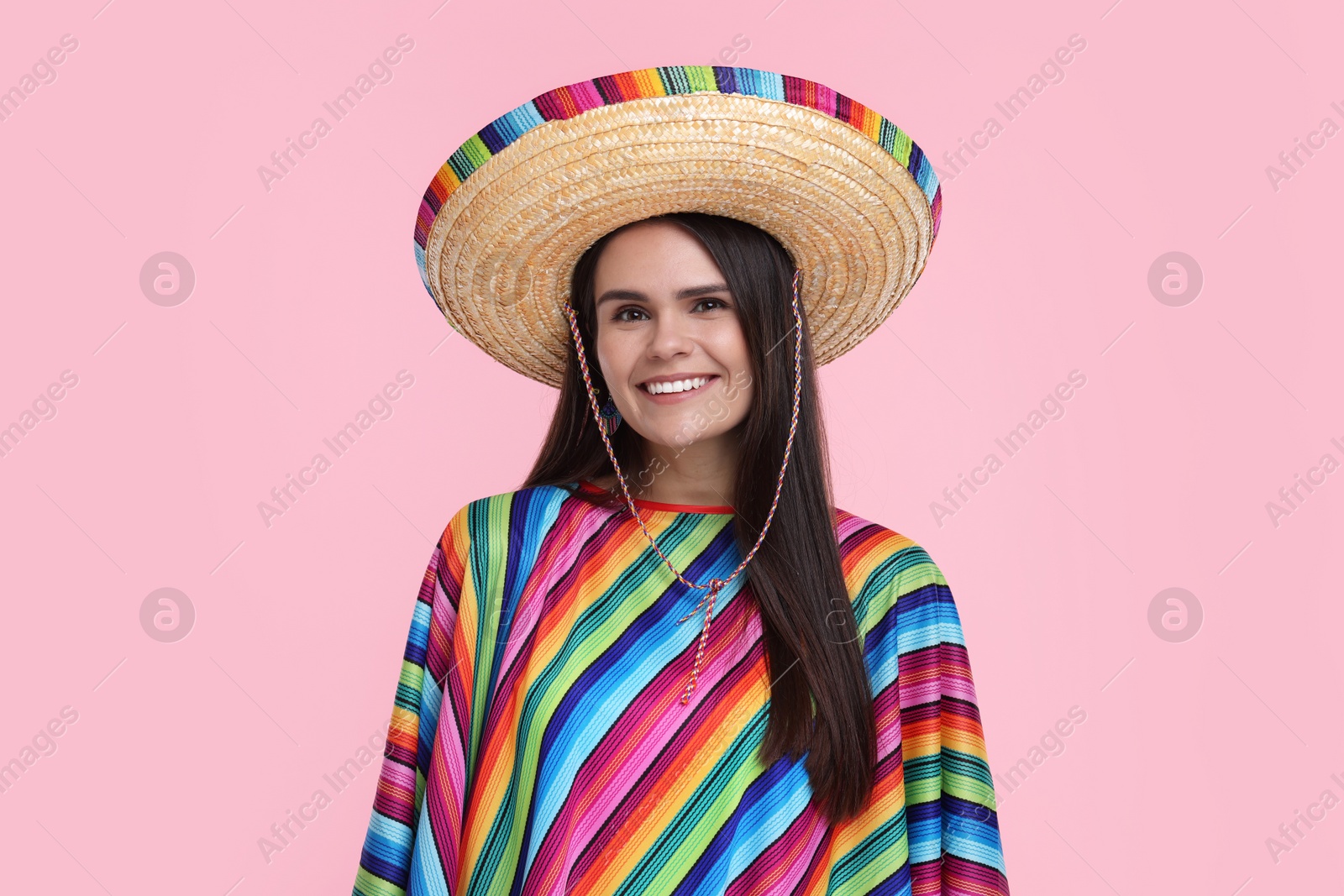 Photo of Young woman in Mexican sombrero hat and poncho on pink background