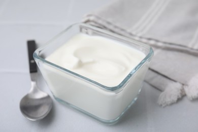 Photo of Delicious natural yogurt in glass bowl and spoon on white table, closeup