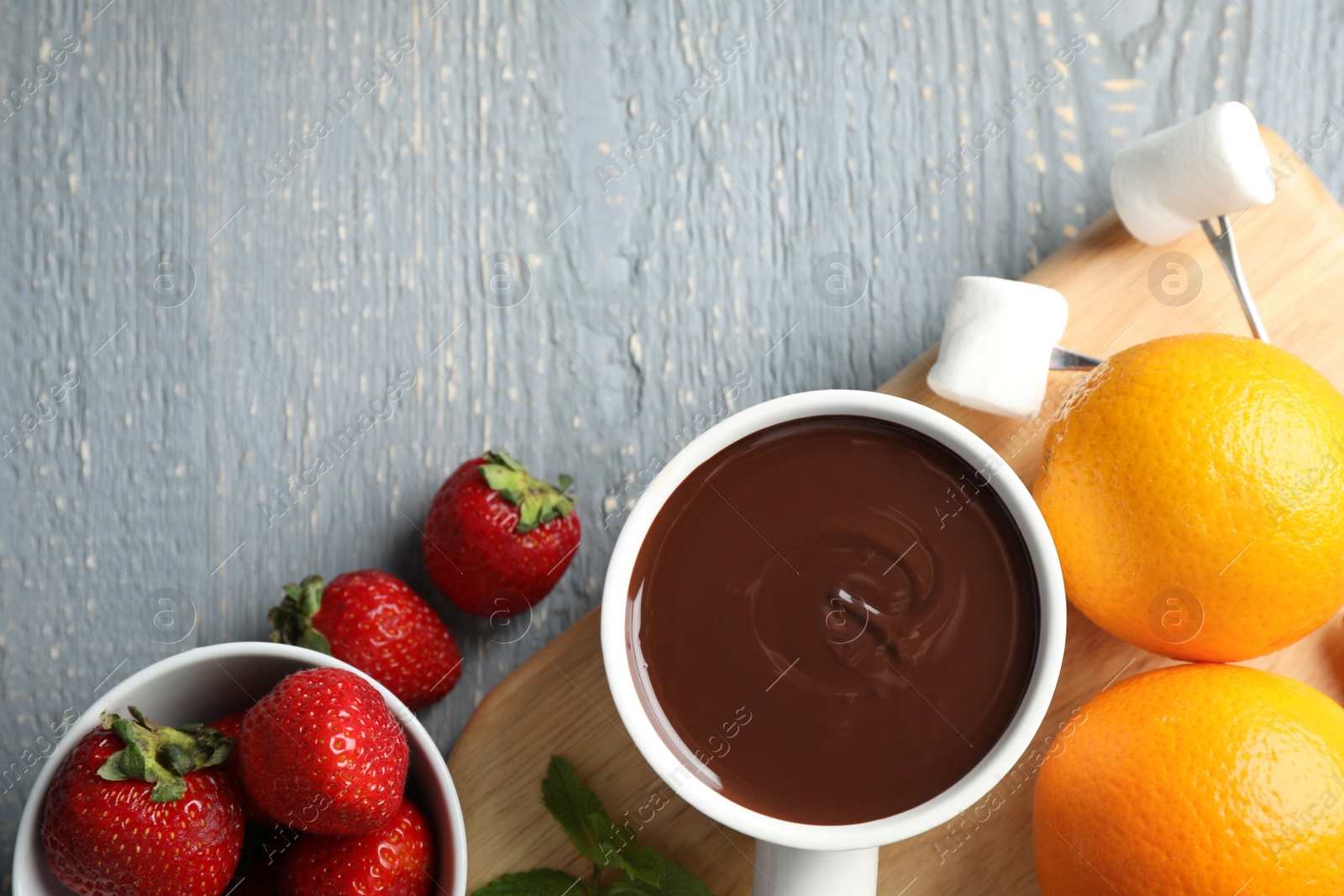 Photo of Flat lay composition with pot of chocolate fondue and fruits on grey wooden table, space for text