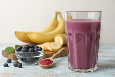 Photo of Fresh acai drink with berries and bananas on wooden table against light background