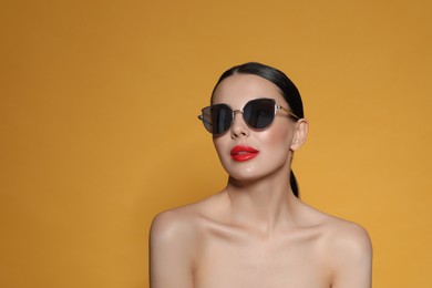 Photo of Attractive woman in fashionable sunglasses against orange background. Space for text