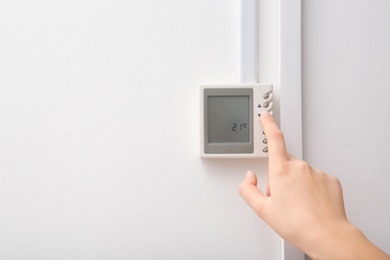 Woman adjusting thermostat on white wall, closeup. Heating system