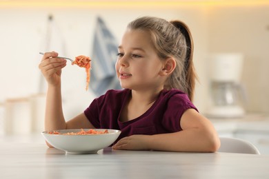 Cute little girl eating tasty pasta at table in kitchen