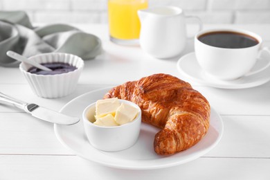 Fresh croissant, butter, jam and coffee on white wooden table. Tasty breakfast