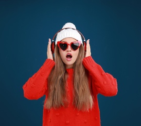 Young woman listening to music with headphones on dark blue background