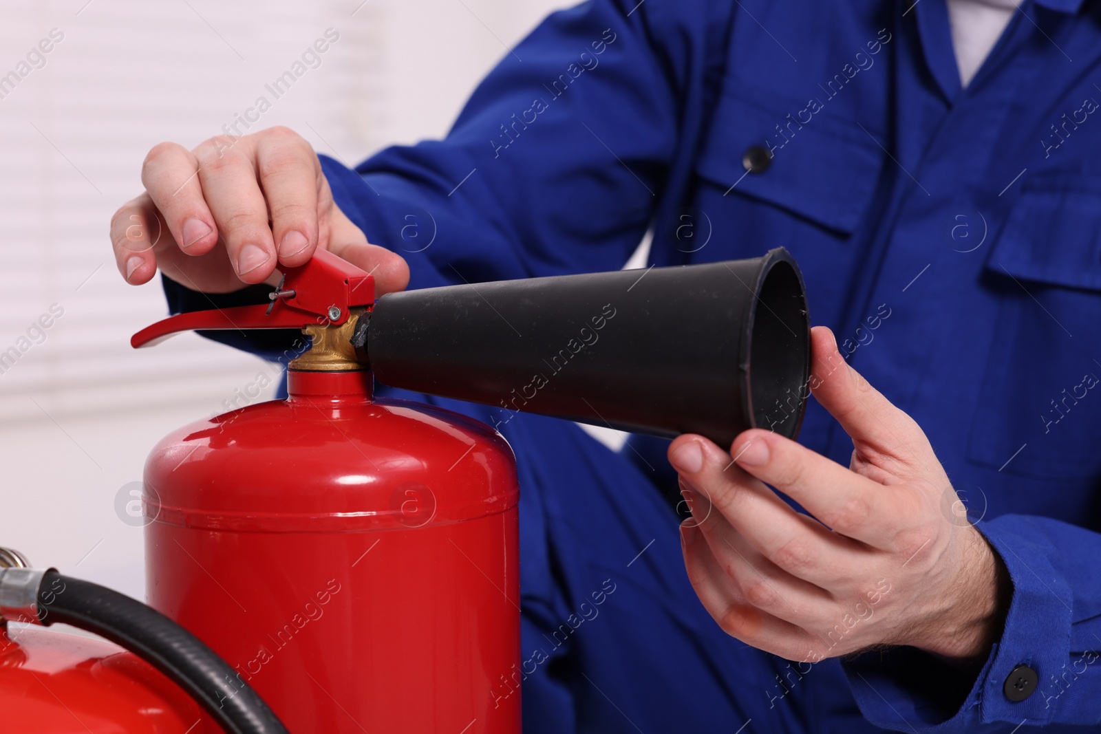 Photo of Man checking quality of fire extinguishers indoors, closeup