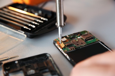 Photo of Technician repairing mobile phone at table, closeup