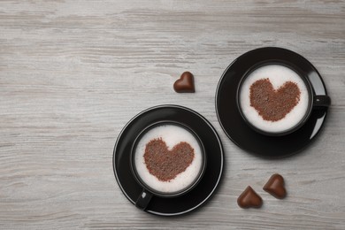Photo of Cups of aromatic coffee with heart shaped decoration and chocolate candies on wooden table, flat lay. Space for text