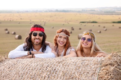 Photo of Happy hippie friends near hay bale in field