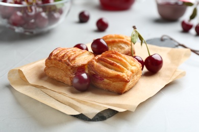 Photo of Fresh delicious puff pastry with sweet cherries served on light table