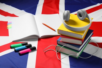 Photo of Learning foreign language. Different books, headphones and stationery on flag of United Kingdom