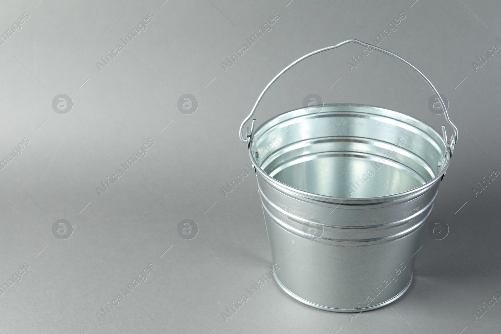 Photo of One shiny metal bucket on light grey background. Space for text