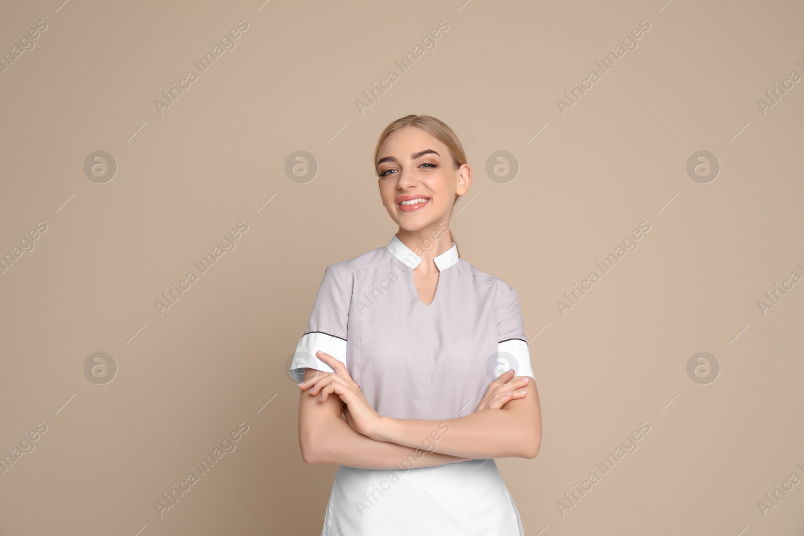 Photo of Portrait of young chambermaid in tidy uniform on color background