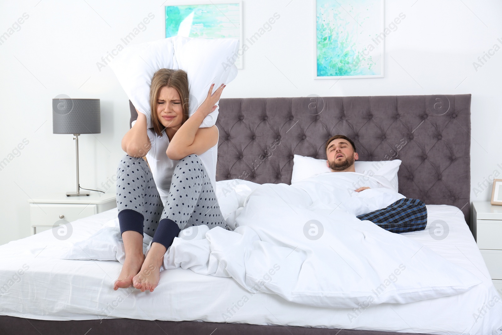 Photo of Upset young woman covering her head with pillow near sleeping husband in bedroom. Relationship problems