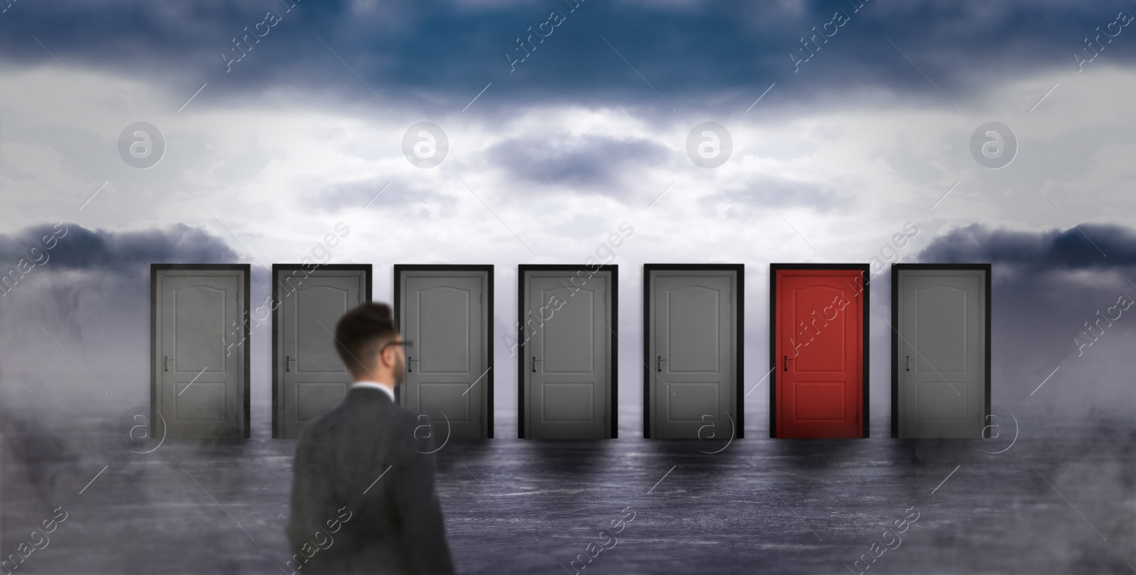 Image of Young man standing in front of many closed doors and sky on background. Choice concept