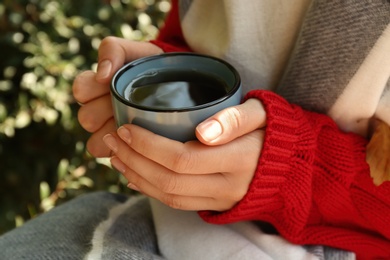 Woman in cozy sweater with cup of hot drink outdoors on sunny autumn day, closeup