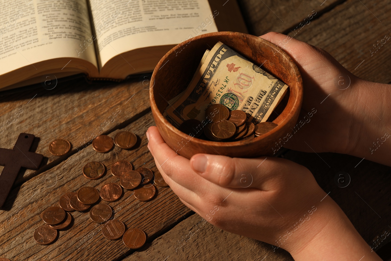 Photo of Donate and give concept. Woman holding bowl with coins and dollar banknotes at wooden table, closeup