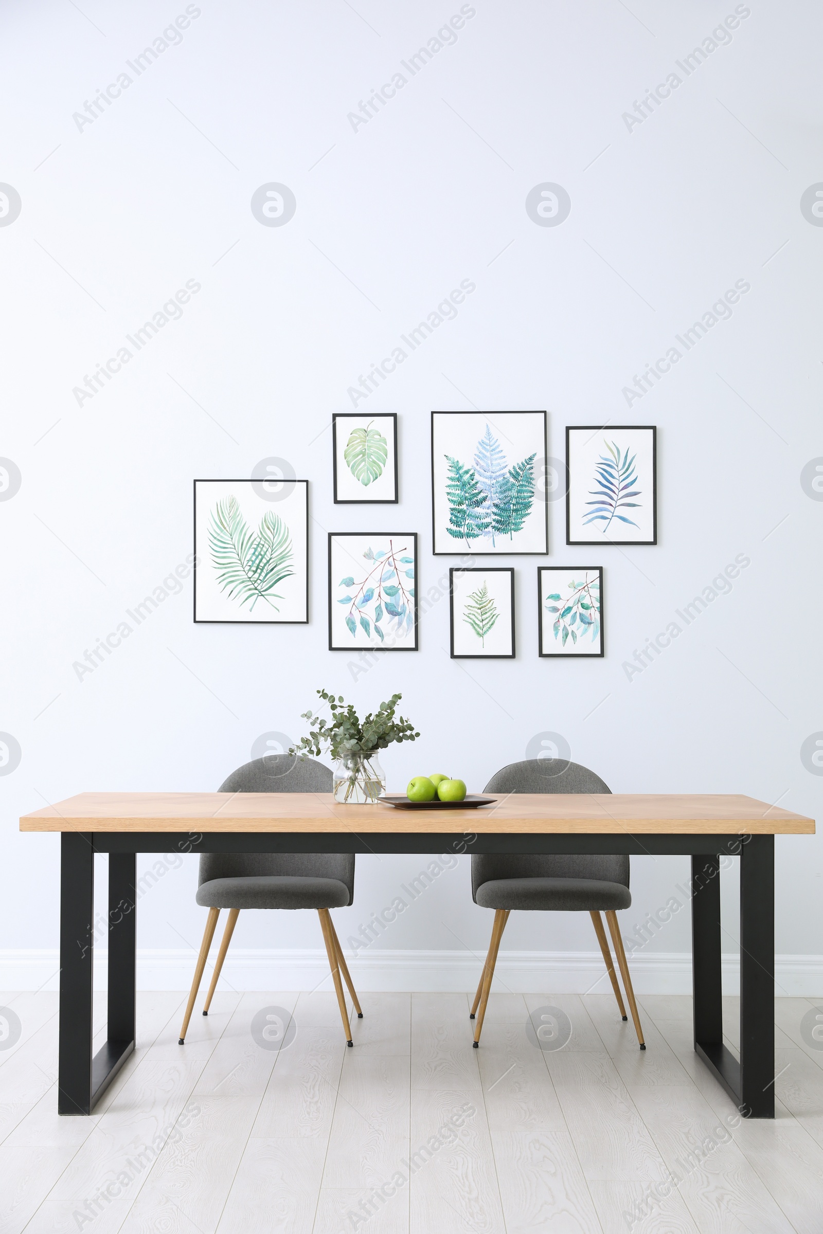 Photo of Stylish room interior with modern table, chairs and paintings of tropical leaves. Idea for design