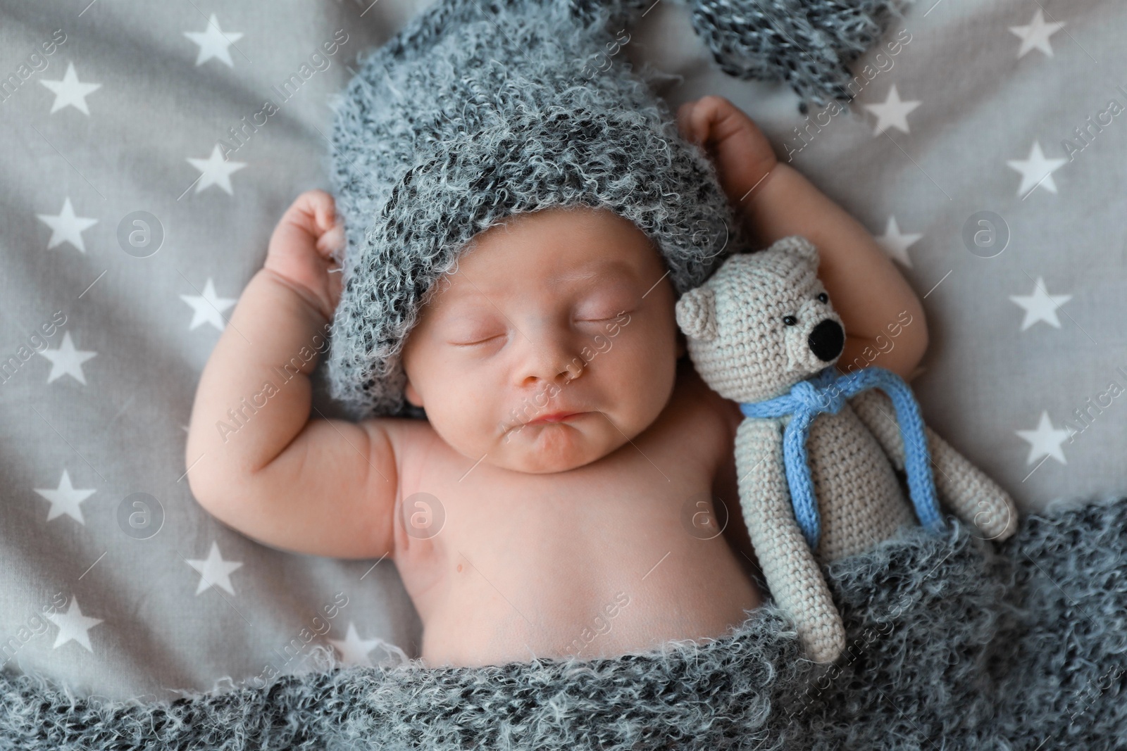 Photo of Cute newborn baby in warm hat with toy sleeping on bed, top view