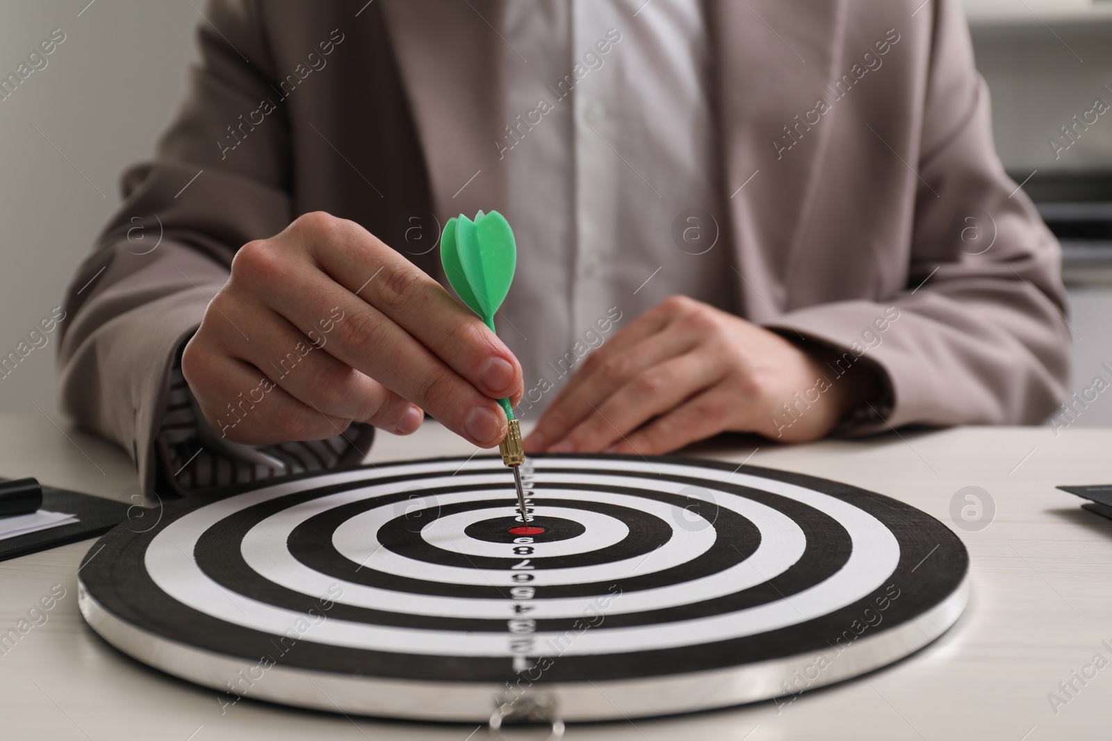 Photo of Business targeting concept. Man with dart aiming at dartboard at table indoors, closeup