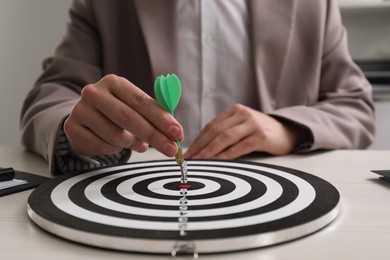 Photo of Business targeting concept. Man with dart aiming at dartboard at table indoors, closeup