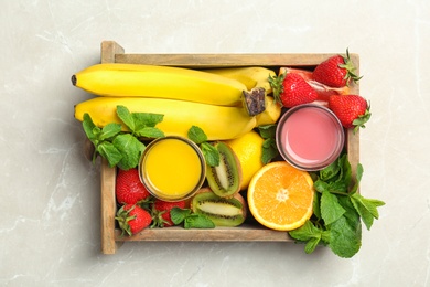 Photo of Wooden crate with tasty juices and ingredients on light background, top view