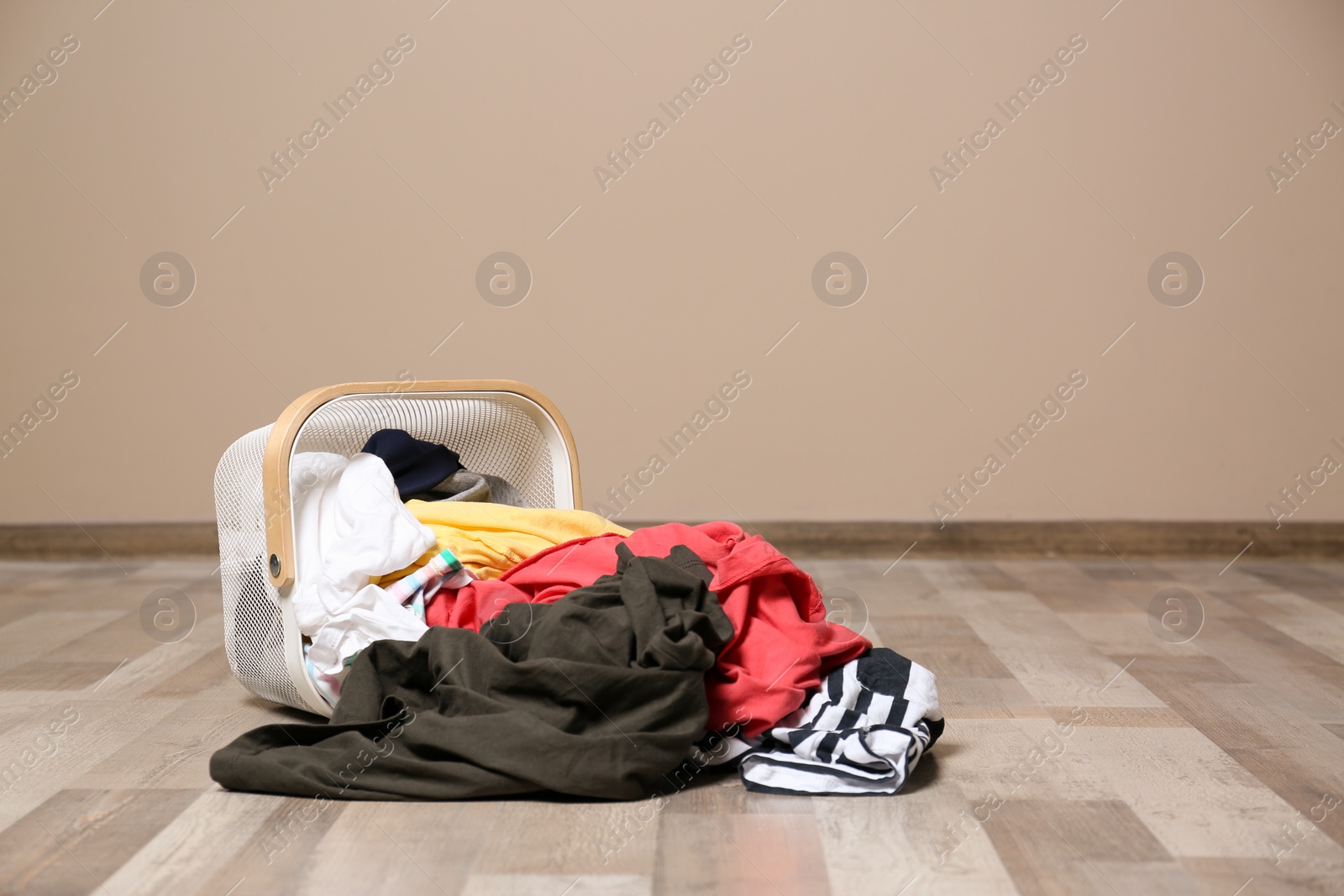 Photo of Dirty clothes scattered from laundry basket on floor indoors. Space for text