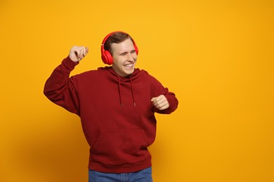 Photo of Handsome young man with headphones dancing on yellow background. Space for text