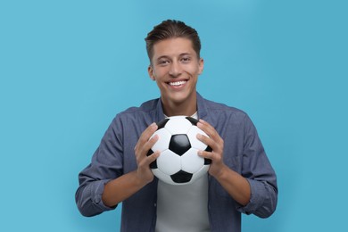 Photo of Happy sports fan with soccer ball on light blue background