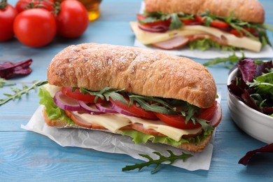 Delicious sandwich with fresh vegetables, cheese and arugula on light blue wooden table