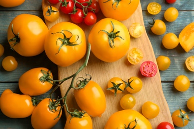 Photo of Ripe yellow and red tomatoes on light blue wooden table, flat lay