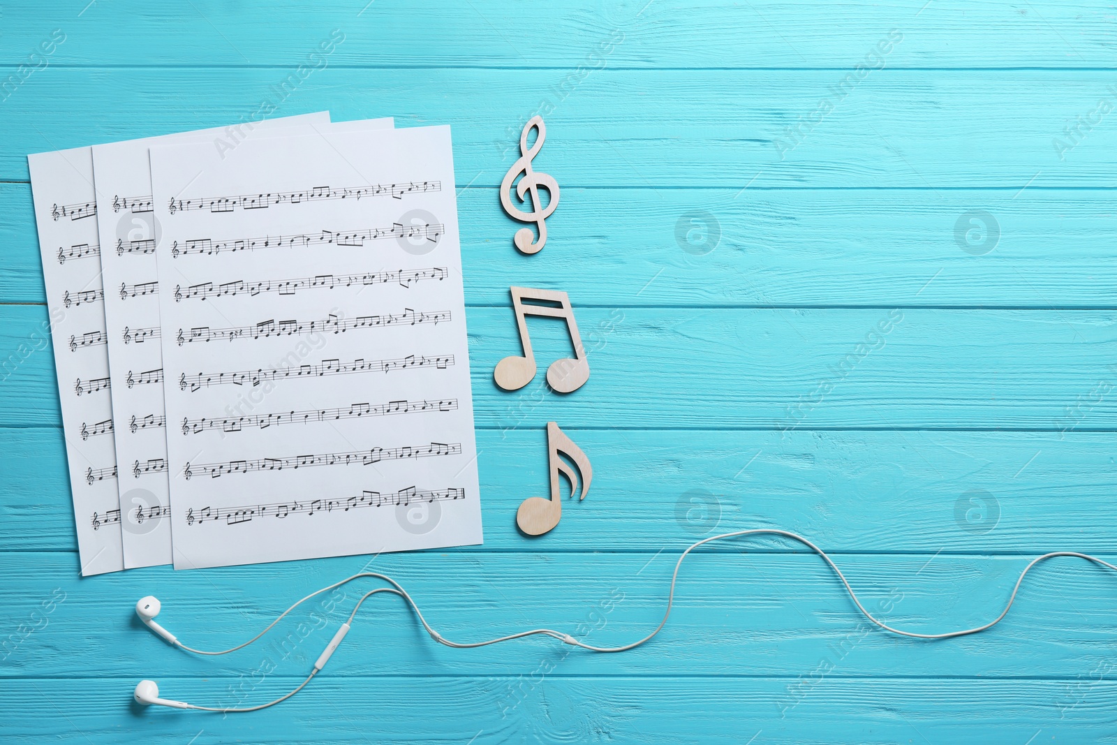 Photo of Earphones, music notes and sheets on wooden background, flat lay. Space for text