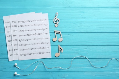 Photo of Earphones, music notes and sheets on wooden background, flat lay. Space for text