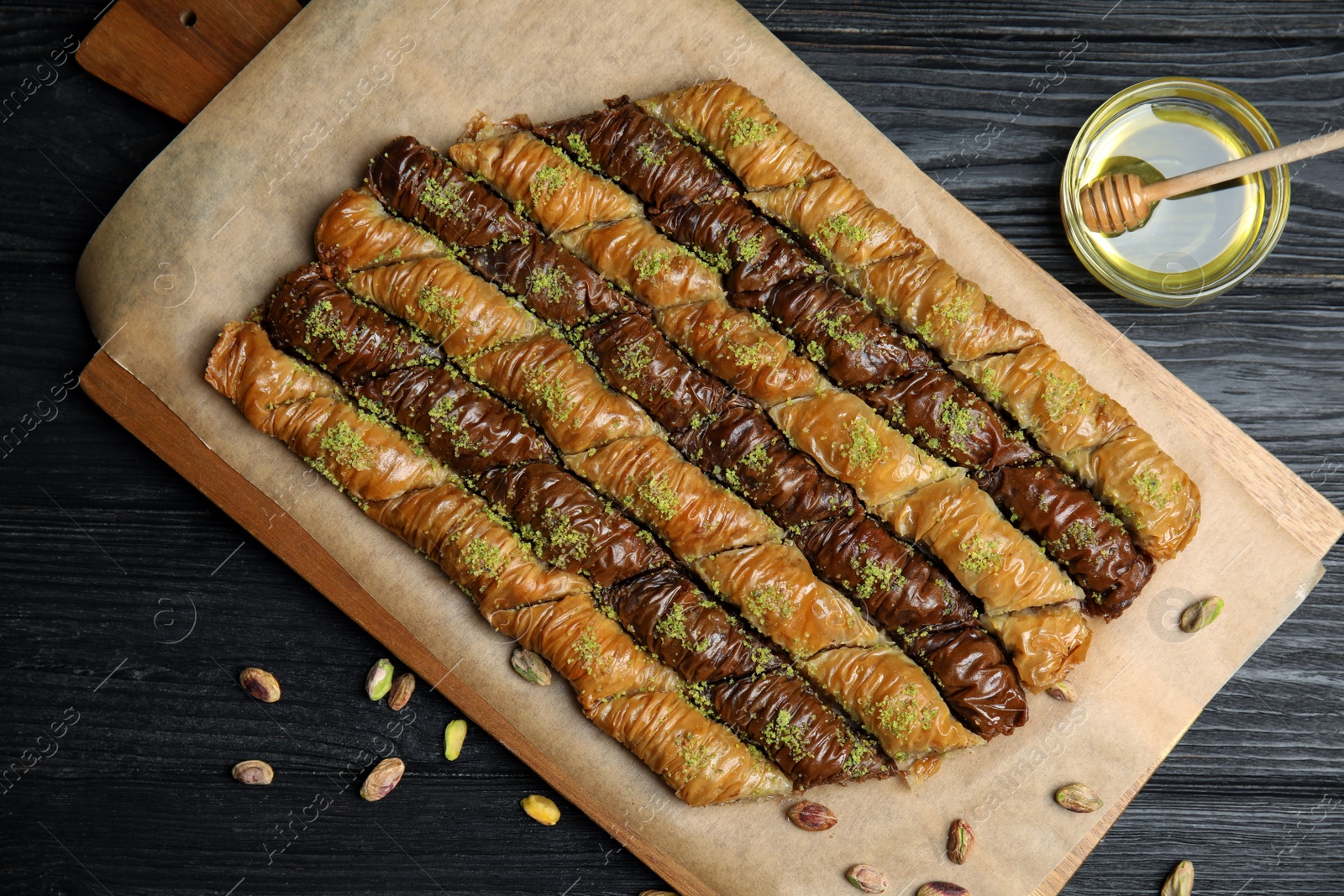 Photo of Delicious sweet baklava with pistachios and honey on black wooden table, flat lay