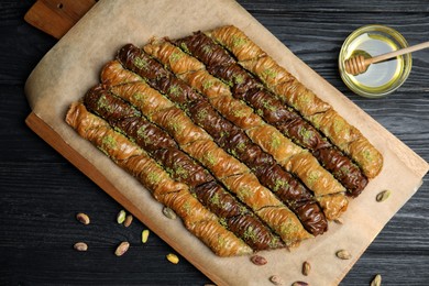 Delicious sweet baklava with pistachios and honey on black wooden table, flat lay