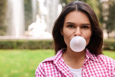 Photo of Beautiful young woman blowing chewing gum outdoors, space for text