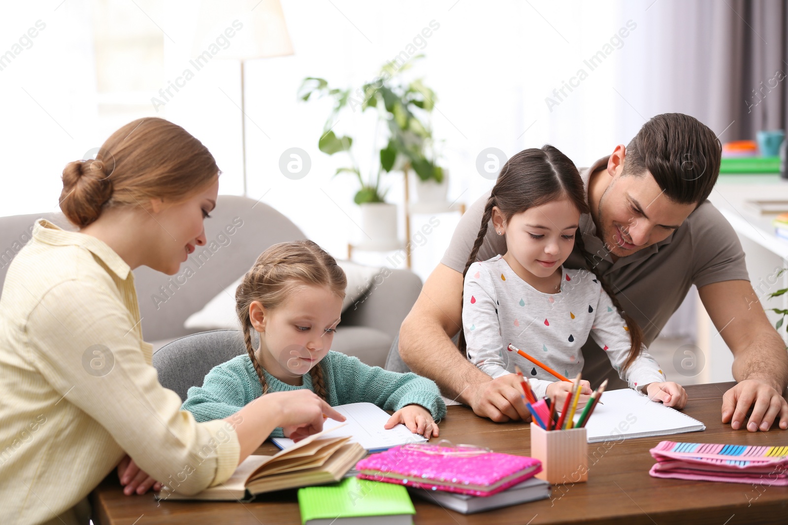 Photo of Parents helping their daughters with homework at table indoors