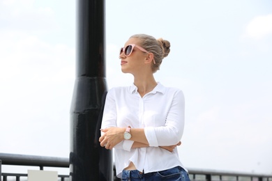 Beautiful young woman with sunglasses standing at pier. Joy in moment