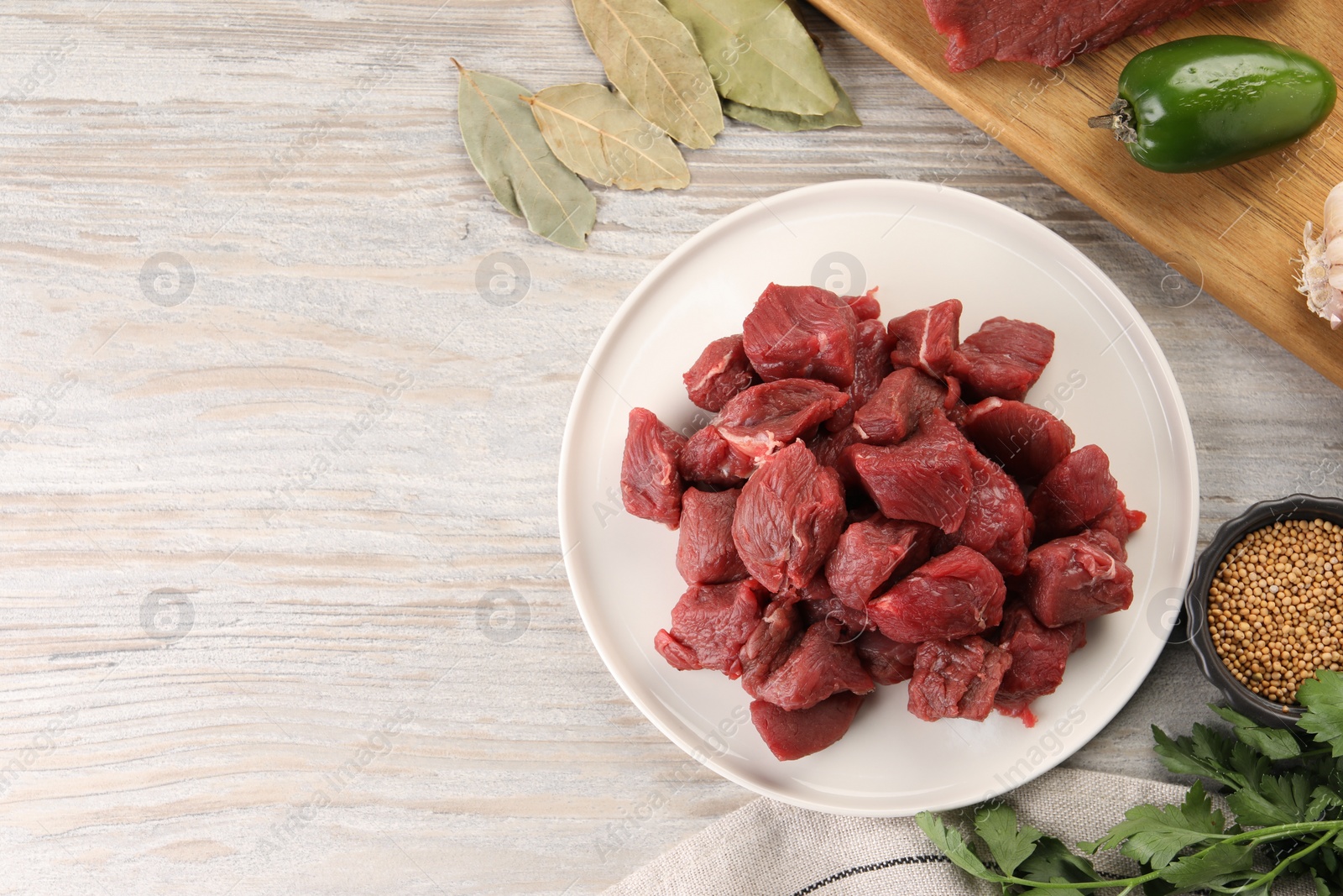 Photo of Pieces of raw beef meat, spices and products on light wooden table, flat lay. Space for text