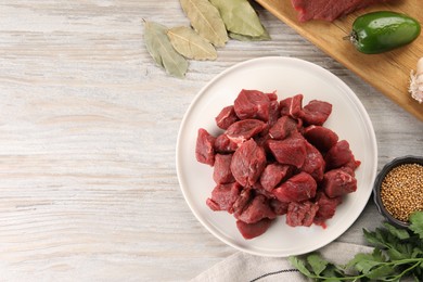 Photo of Pieces of raw beef meat, spices and products on light wooden table, flat lay. Space for text