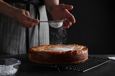 Woman decorating tasty apricot pie with powdered sugar at black table, closeup