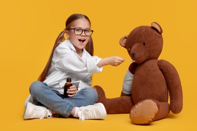 Little girl playing doctor with toy bear on yellow background