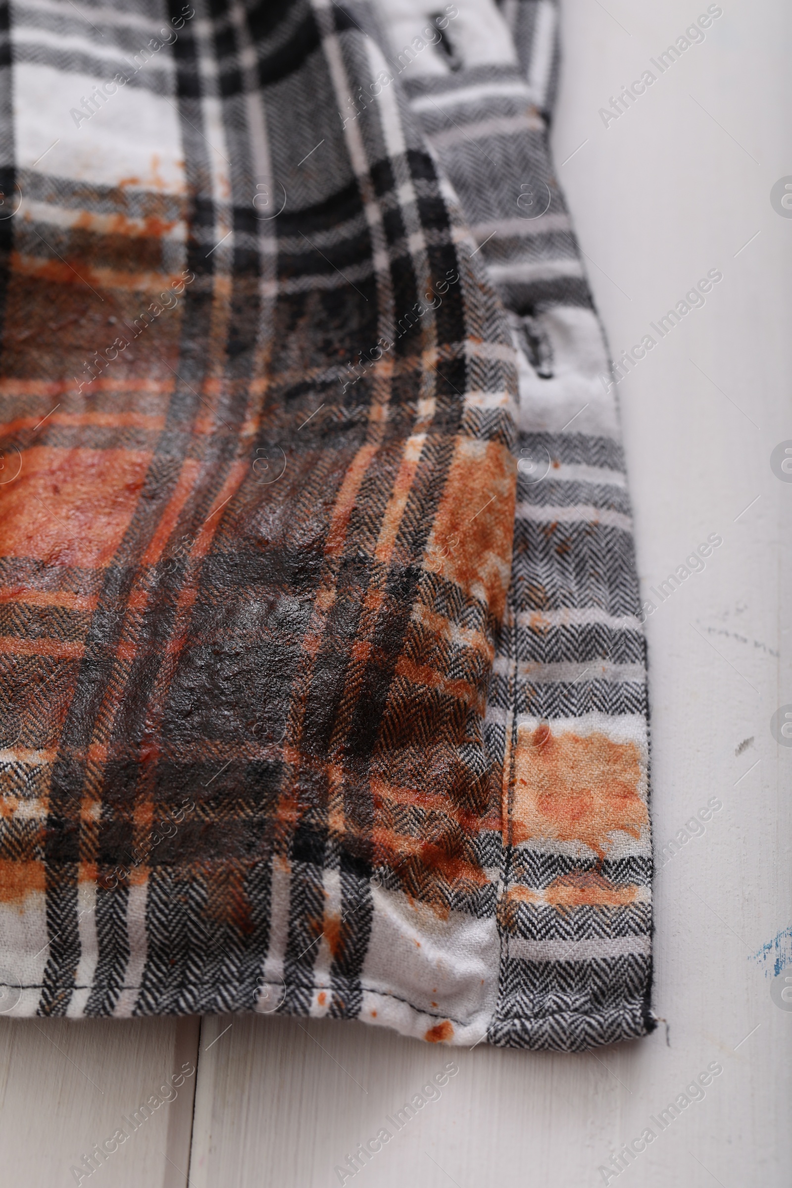 Photo of Shirt with stain of sauce on white wooden table, closeup