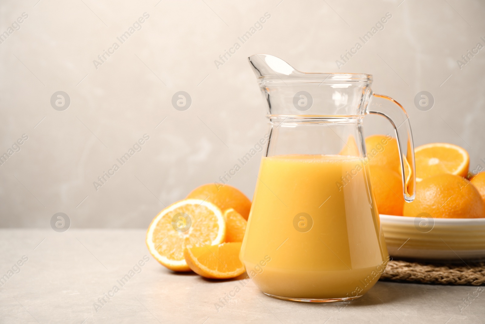 Photo of Jug of orange juice and fresh fruits on light grey table. Space for text