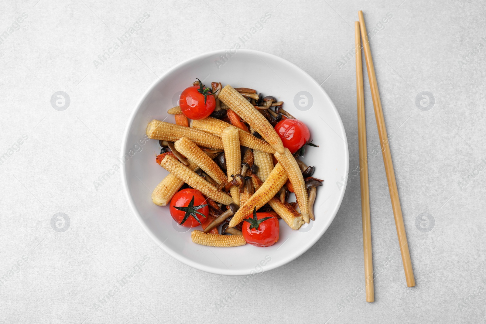 Photo of Tasty roasted baby corn with tomatoes, mushrooms and chopsticks on light grey table, flat lay