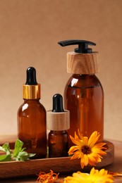 Bottles of essential oils and beautiful calendula flowers on wooden table