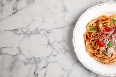 Tasty pasta with tomatoes, cheese and basil on white marble table, top view. Space for text